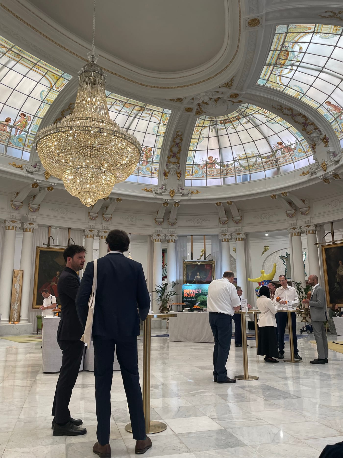 Interior of the Argus Europe Carbon Conference 2026 venue in Nice — a Belle Époque hall with a large crystal chandelier hanging beneath a domed stained-glass ceiling, with attendees networking around exhibition stands